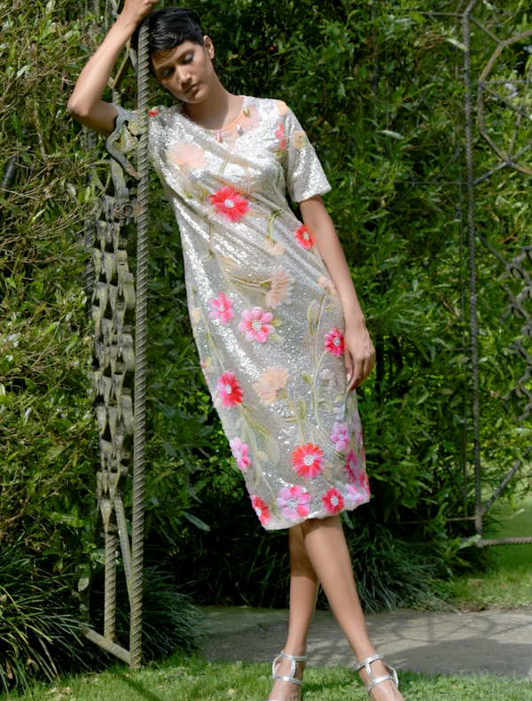 A woman in a silver and pink floral dress leans against a tree, enjoying a serene moment in nature.