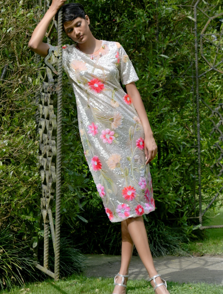 A woman in a silver and pink floral dress leans against a tree, enjoying a serene moment in nature.