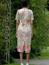 A woman in a silver and pink floral dress stands gracefully in a vibrant garden filled with blooming flowers.