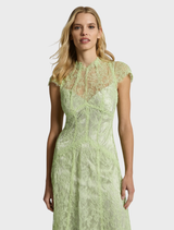 A woman stands in a garden wearing a citrus lace midi dress, surrounded by colorful flowers and lush greenery.