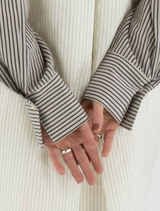 Grey Mira blouse draped on a hanger, featuring a modern silhouette and smooth texture.