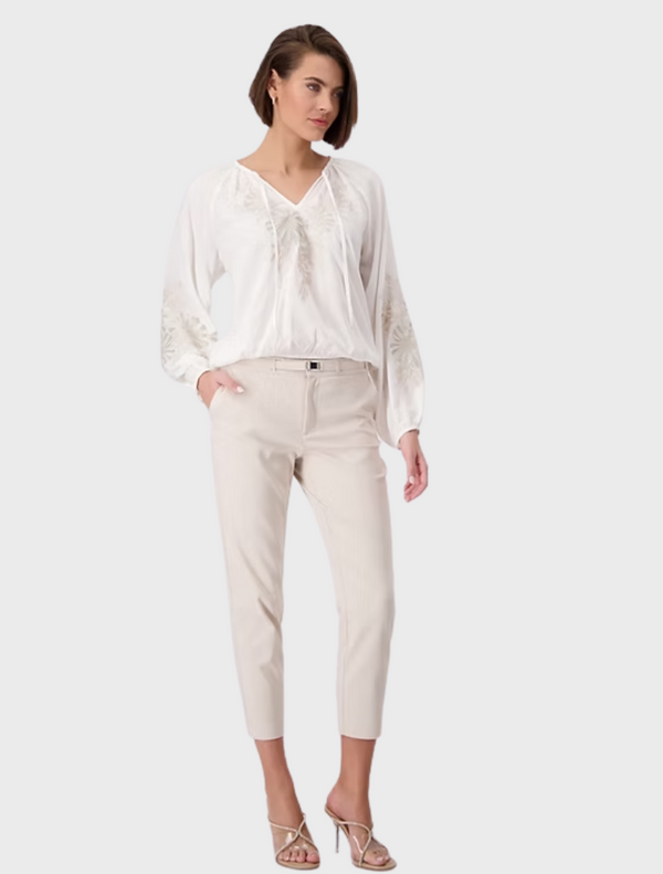 A model showcases a white blouse paired with matching white pants, presenting a chic and elegant outfit.