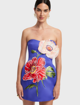 A woman wearing a blue dress adorned with a vibrant flower print, standing confidently with a smile.