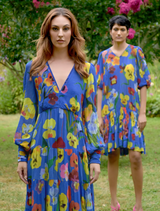 Two women in cobalt floral dresses stand in a grassy area, enjoying a sunny day outdoors.