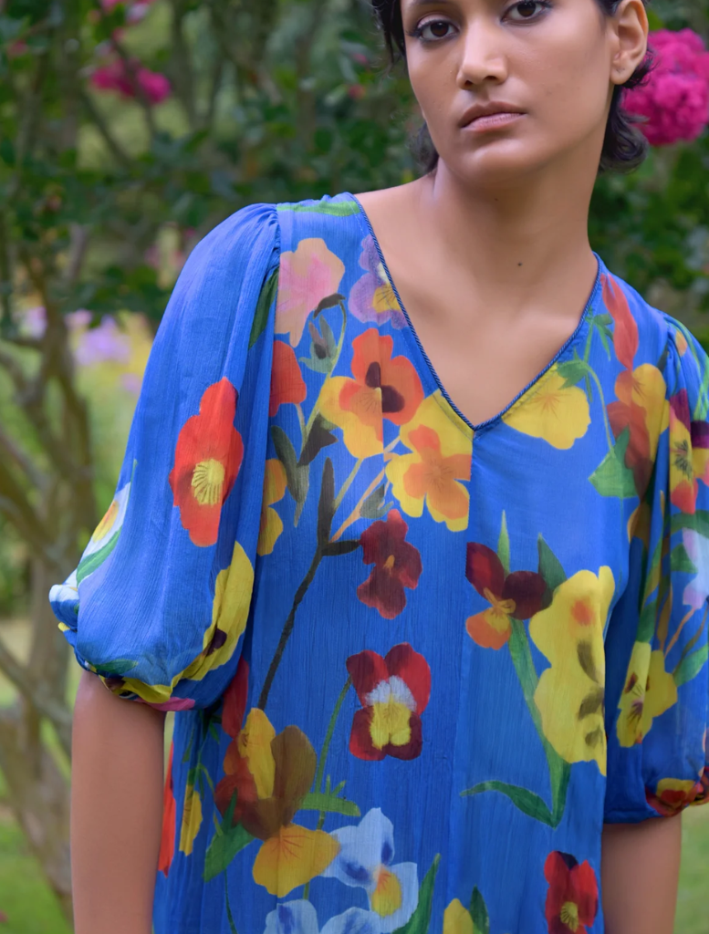 A woman in a bright floral dress stands next to a tree, highlighting the Sweet Nothing Tunic's vibrant design.