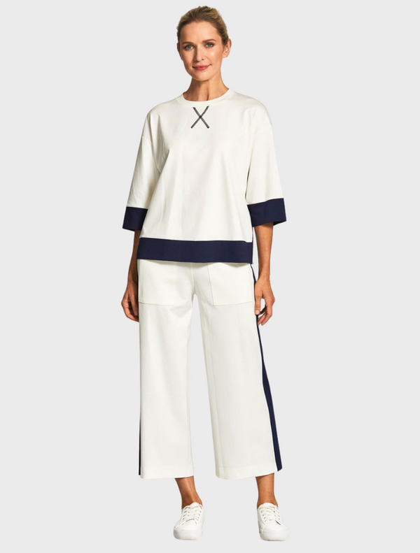 A model is dressed in a white top paired with navy pants, showcasing a stylish and modern outfit.