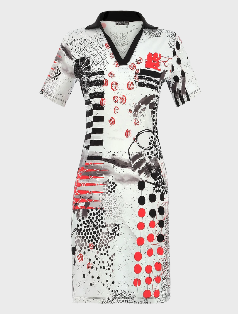 A woman dressed in a white polka dot dress with red and black accents stands, exuding elegance and charm.