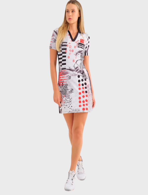A woman wearing a white dress adorned with red and black polka dots stands confidently, showcasing her stylish outfit.