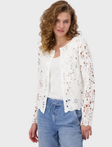A woman wears a white lace top paired with blue jeans, presenting a casual yet elegant look.