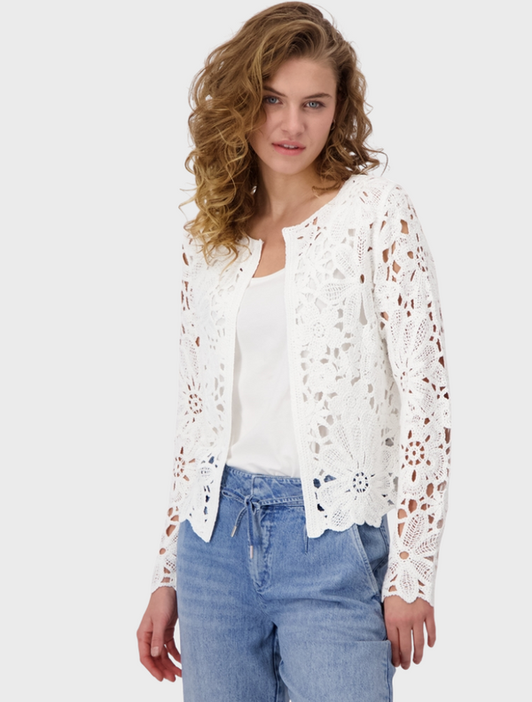 A woman wears a white lace top paired with blue jeans, presenting a casual yet elegant look.