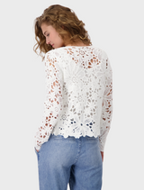 A woman showcases a white lace top and blue jeans, combining elegance with casual style.