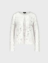 A woman in a white lace top and blue jeans stands, exemplifying a chic and relaxed fashion choice.
