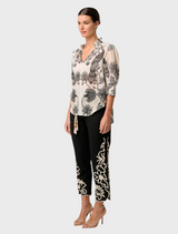 A woman in a floral blouse with a shirred collar paired with a black skirt, representing the Oleander Placement Print.