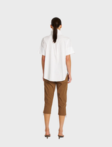 A woman in a white shirt and brown cropped zip cargo pants smiles while standing outdoors.