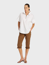 A woman wearing a white shirt and brown cropped zip cargo pants stands confidently.