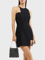 A woman in a stylish black dress and heels poses on a street, accessorized with a black Kit Crystal Cage Bag.