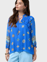 Azure multi-printed blouse featuring blouson sleeves, elastic cuffs, ruffles on front and back, and a glass bead tie neckline.
