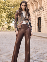 A woman models a dark brown and black knit jacket paired with brown leather pants.