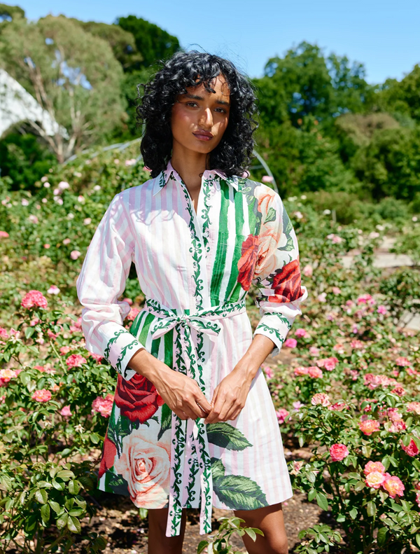 A woman in a floral dress stands in a garden, showcasing the Demi Dress in Leaf Rose Multi against vibrant greenery.