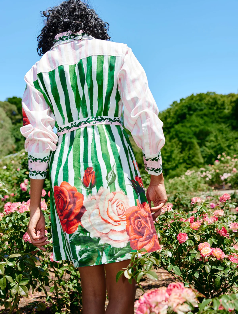A woman stands gracefully in a garden, dressed in the floral Demi Dress - Leaf Rose Multi, surrounded by vibrant foliage.
