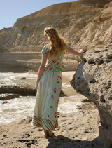 A woman in a floral dress stands on a rocky beach, showcasing the Tillla Denim Maxi Skirt in Meadow Multi.