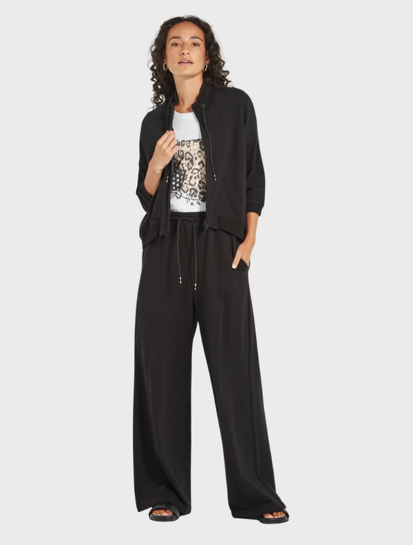  A model poses in black pants and a white top, showcasing a stylish and modern outfit.
