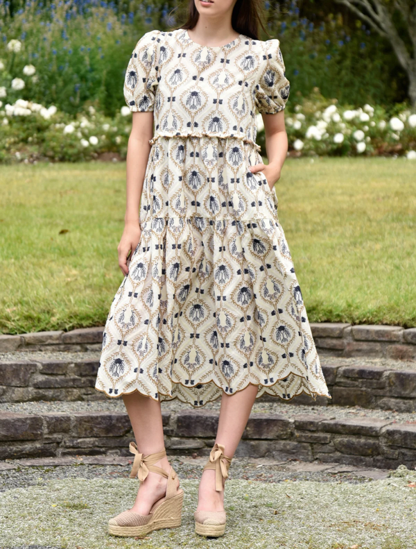 A young woman in a floral-patterned dress stands, showcasing the vibrant colors and design of her outfit.