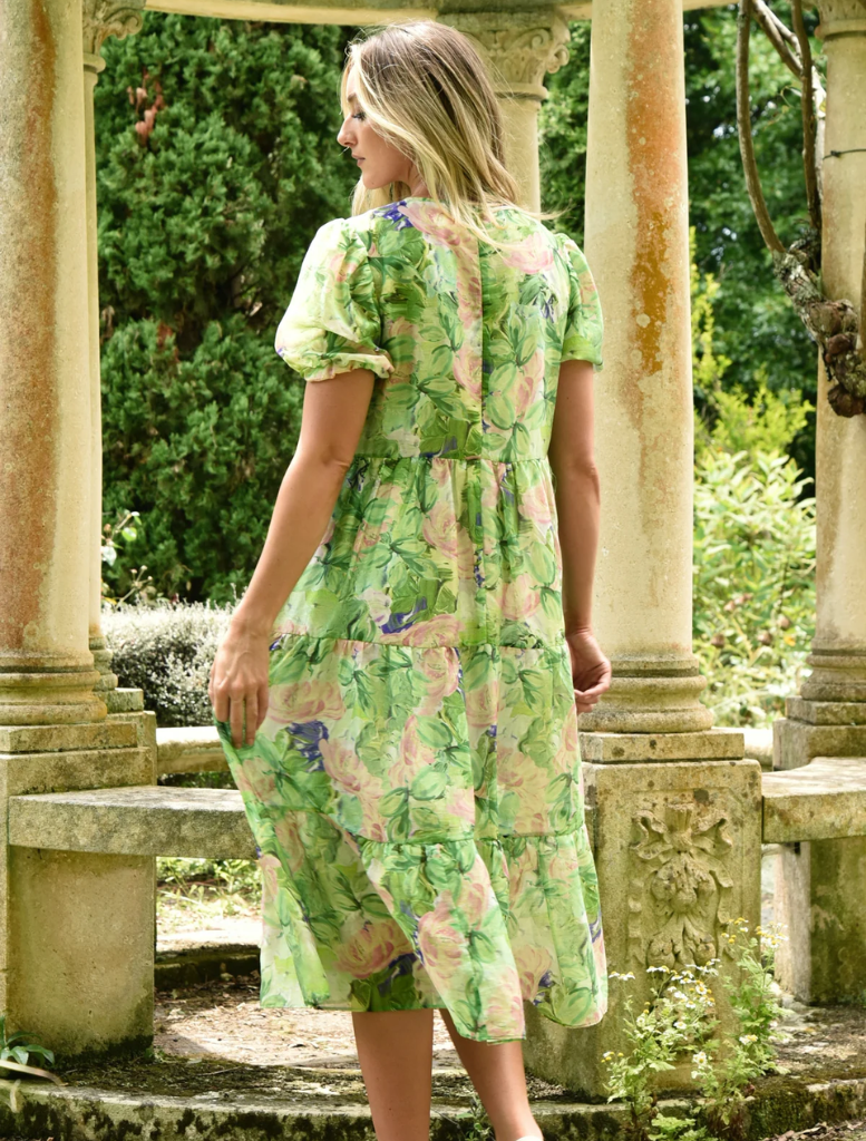 A woman in a flowing green dress stands before a stone archway, creating a striking contrast between fabric and stone.