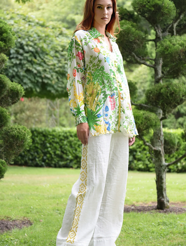 A woman wearing a floral Shirt walks leisurely in a park, enjoying the natural scenery around her.