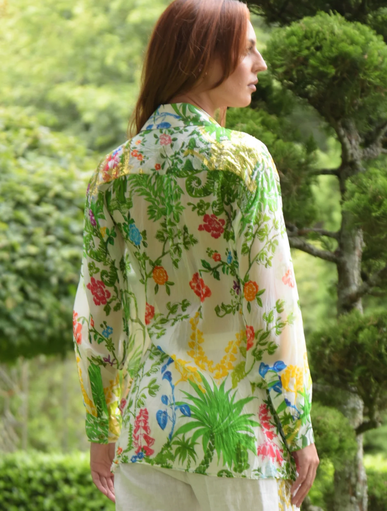 A woman in a floral Shirt strolls through a park, surrounded by greenery and blooming flowers.