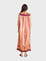 Back view of a woman in a long orange and pink patterned dress, showcasing the vibrant colors and flowing design.