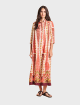 A woman models a long orange and white patterned dress, showcasing its vibrant colors and flowing design.