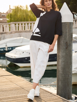 A woman dressed in white pants and a blue top poses, highlighting her fashionable and relaxed attire.