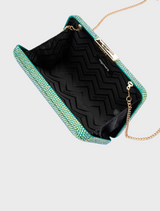 A blue glitter clutch bag, identified as the Edith Iridescent Clutch - Green, hanging from a delicate chain strap.