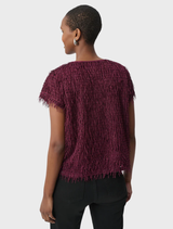 A woman seen from the back, wearing a purple top, stands against a neutral background.