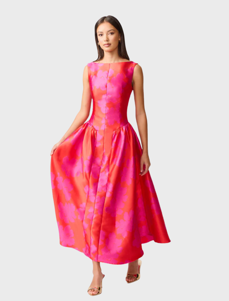 A woman in a pink and red dress poses elegantly, embodying a chic and colorful fashion statement.