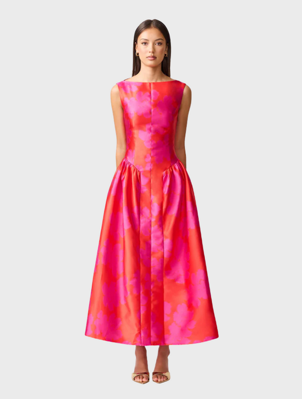 A woman wearing a pink and red dress stands gracefully, showcasing the vibrant colors and elegant design of her outfit.