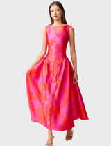A woman wearing a pink and red dress stands gracefully, showcasing the vibrant colors and elegant design of her outfit.