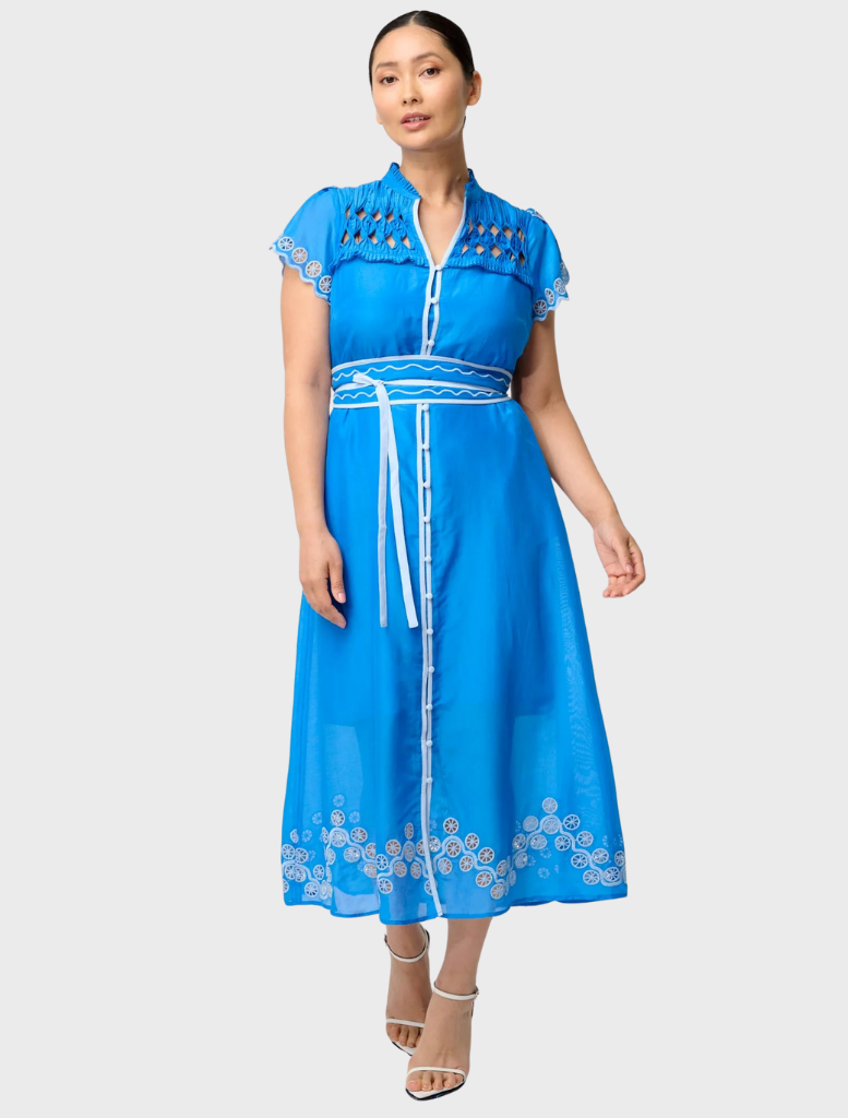 A woman in a blue dress with a white collar, featuring intricate embroidery, styled as the Petite Xanthia Diamond Smock.
