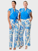 A woman in a blue and white floral dress, featuring the Thalassa Embroidered Silk Cotton Flutter Sleeve Top in Blue Topaz.