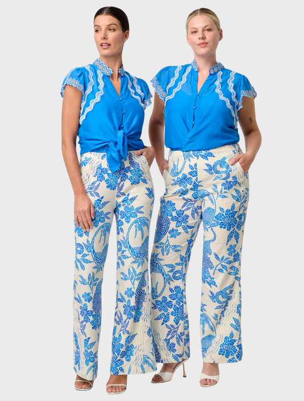 A woman in a blue and white floral dress, featuring the Thalassa Embroidered Silk Cotton Flutter Sleeve Top in Blue Topaz.