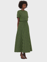 A woman wearing a green and black checkered dress stands confidently, showcasing her stylish outfit.