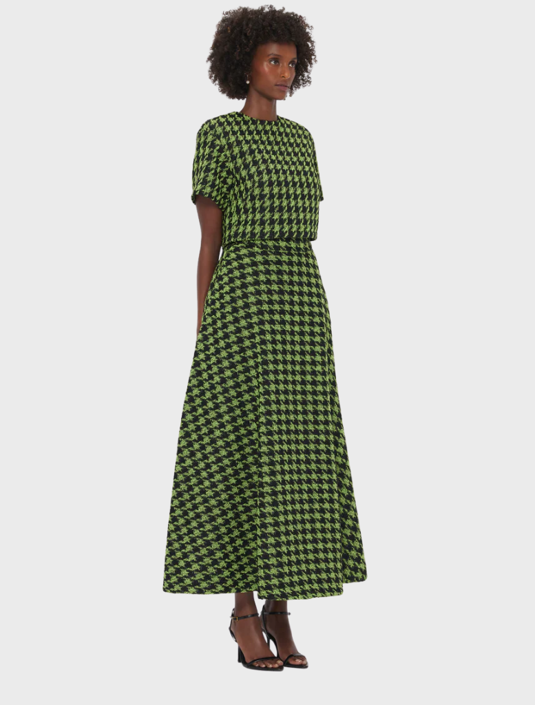 A woman wearing a green and black checkered dress stands confidently, showcasing her stylish outfit.