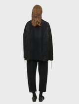 Black oversized jacket, unisex design, made from wool-blend brocade and flannel, featuring two pockets and decorative cords.