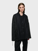 Unisex oversized black jacket crafted from wool-blend brocade and flannel, with two pockets and decorative cord details.