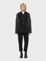 Black unisex oversized jacket made of wool-blend brocade and flannel, featuring two front pockets and decorative cords.
