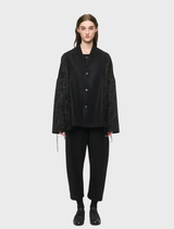 Unisex black oversized outerwear in wool-blend brocade and flannel, with two front pockets and decorative cords on seams.