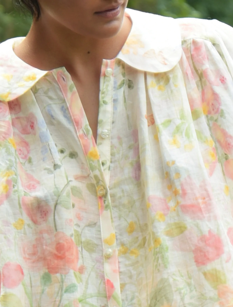 A woman dressed in a floral pattern walks along a path in a park, with lush greenery surrounding her.