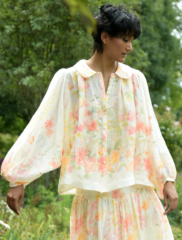 A woman in a floral dress strolls through a park, surrounded by greenery and blooming flowers.