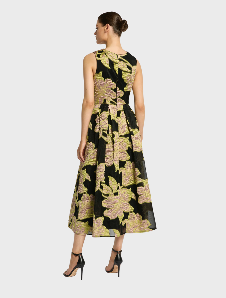 Woman wearing a sleeveless black midi dress with large pink and green floral print, paired with black high-heeled sandals, shown from the back.